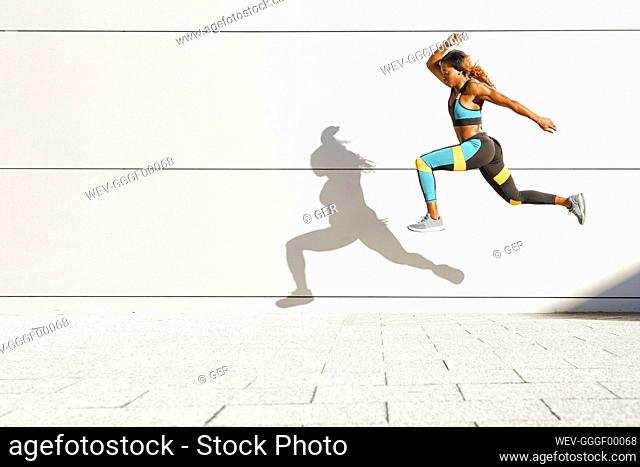 Young woman running against white wall at city