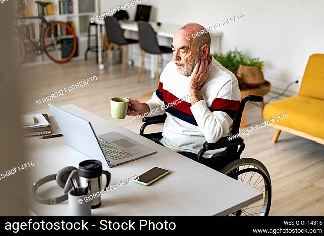 Businessman holding coffee cup on wheelchair at desk