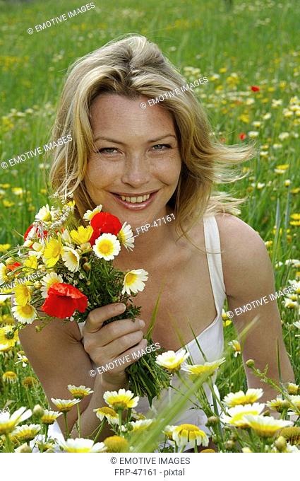 Woman is sitting in a meadow with a bunch of flowers