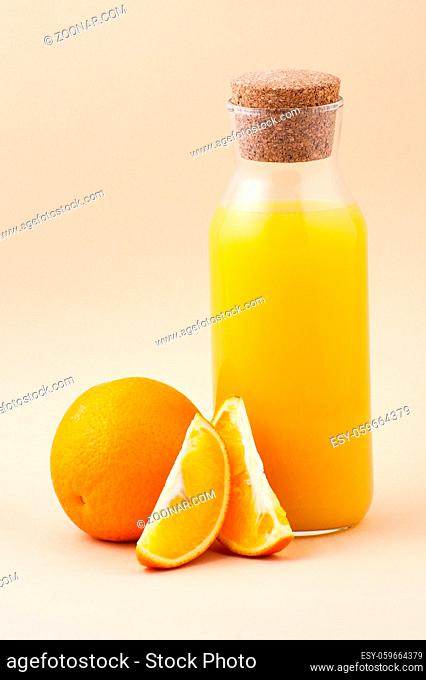 Fresh orange juice in a glass bottle and orange on a light beige background