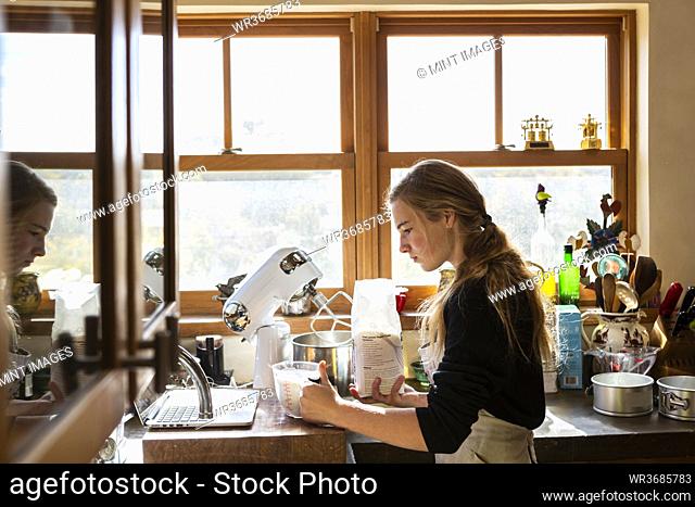 Teenage girl in a kitchen following a baking recipe on a laptop