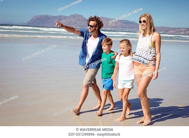 Happy man pointing away with family walking at beach