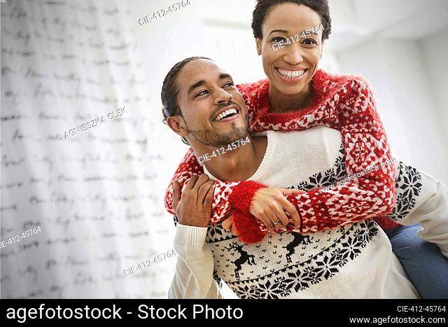 Portrait happy, playful couple in Christmas sweaters piggybacking