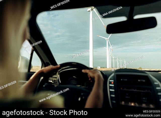Hands of woman driving car at wind park