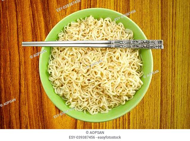Noodles in bowl and chopsticks on wood background