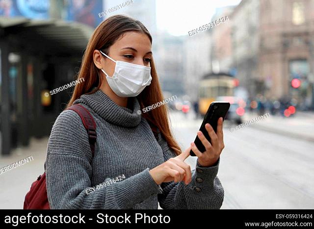 Student teenager girl with protective mask paying for online transport ticket via banking application on smartphone in city street