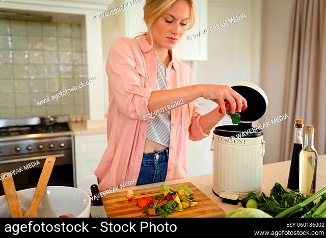 Caucasian woman standing in kitchen preparing food, composting vegetable waste