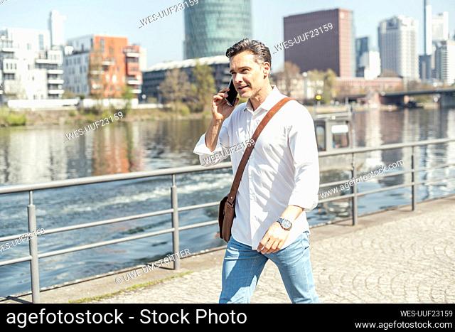 Businessman with crossbody bag talking on mobile phone during sunny day