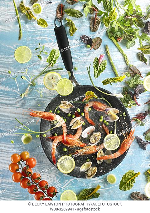 Composition with vegetables and seafood, flying over a frying pan, with blue background