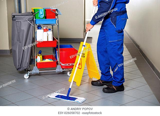 Low section of male janitor with broom cleaning office corridor