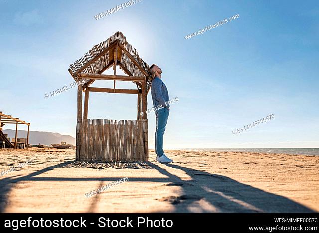 Mid adult man with hands in pockets relaxing while leaning on wooden stall