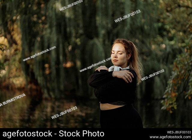 Woman with eyes closed hugging self in park