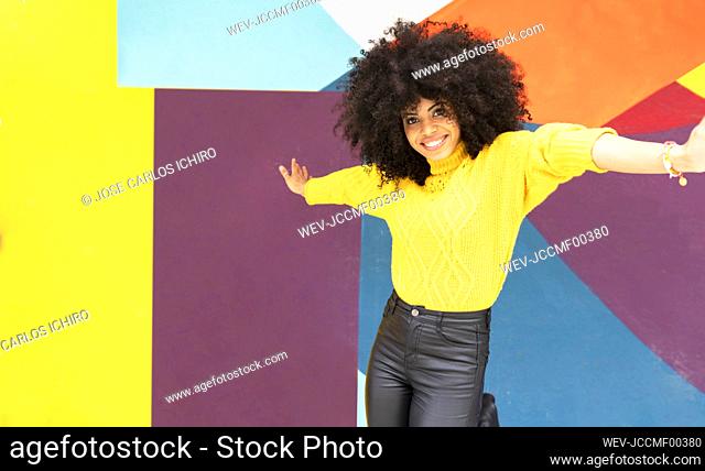 Carefree woman dancing with arms outstretched against multi colored wall
