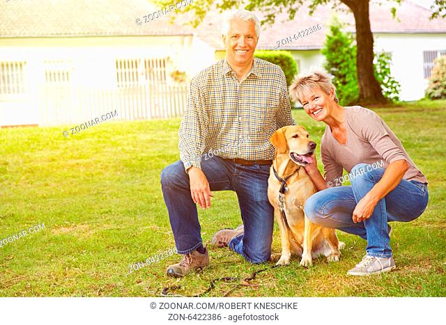 Glückliches Paar Senioren sitzt vor einem Haus mit einem Labrador Retriever