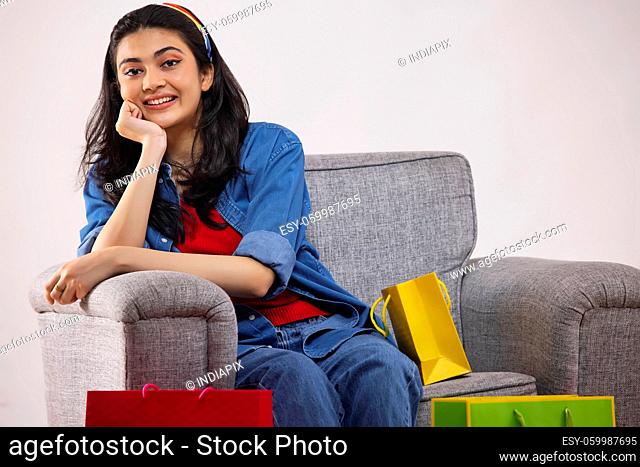 A young woman sitting on a sofa with Colorful shoppingbags in her room