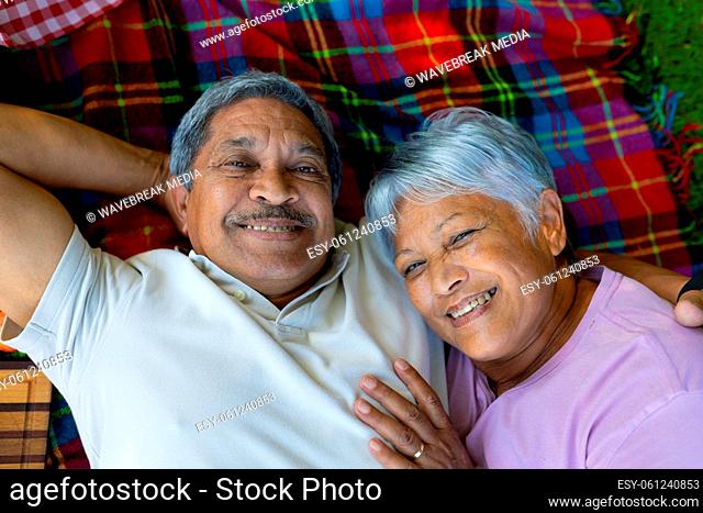 High angle portrait of smiling biracial senior couple lying on blanket while enjoying picnic in park