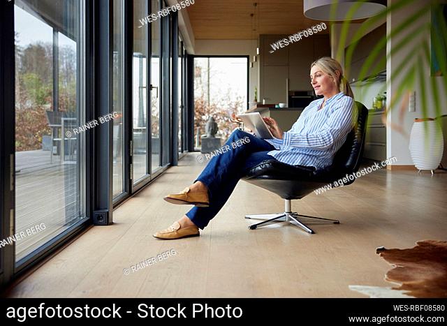 Blond woman using tablet PC sitting on chair at home