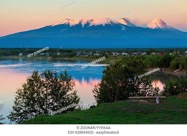 Sunset lighting Kluchevskaya group of volcanoes with reflection in river Kamchatka