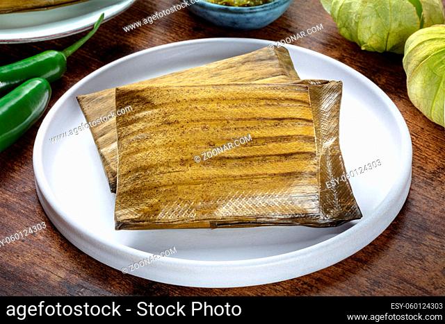 Tamale, traditional dish of the cuisine of Mexico, various stuffings wrapped in green leaves. Hispanic food. With chili peppers and tomatillos
