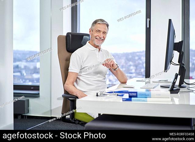 Portrait of smiling doctor sitting at desk in medical practice