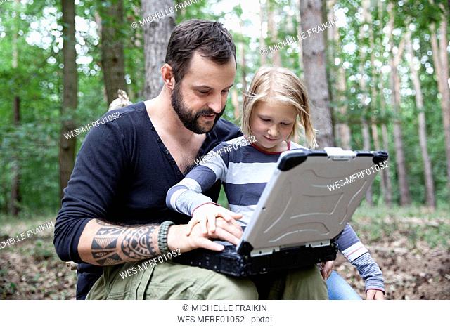 Father and daughter in forest using laptop