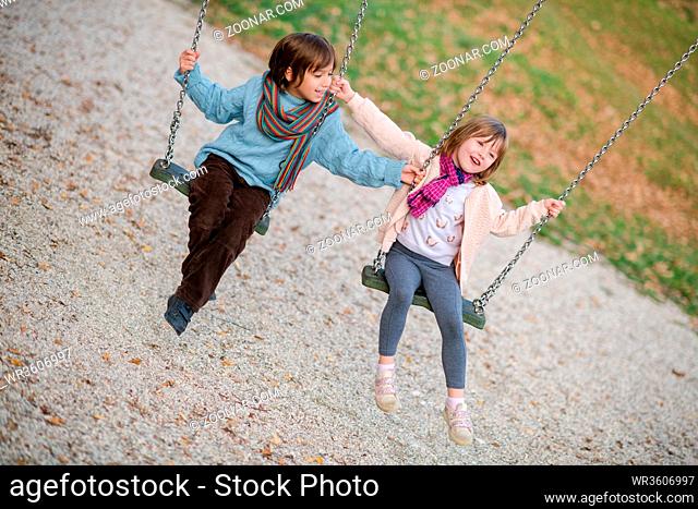 cheerful children are having fun on a swing little brother and sister playing outside