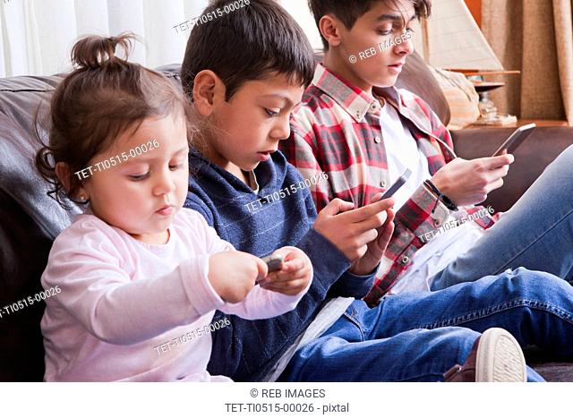 Siblings using smart phones on sofa