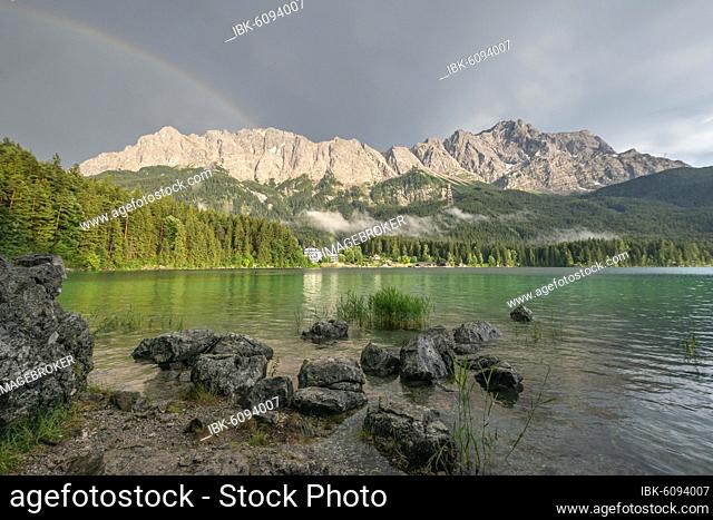Rocks on the shore, Eibsee lake in front of Zugspitze massif with Zugspitze with rainbow, behind thunderclouds, Wetterstein range, near Grainau, Upper Bavaria