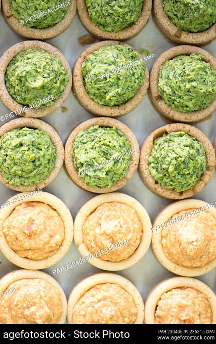 06 April 2023, Saxony, Dresden: Round dough molds made from field bean flour filled with a pea and wild garlic paste (above) and a paprika and feta paste lie on...