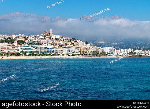 View over the ocean on the city of Altea with blue domed church along Costa Blanca coast with cloudy mountainrange, Spain