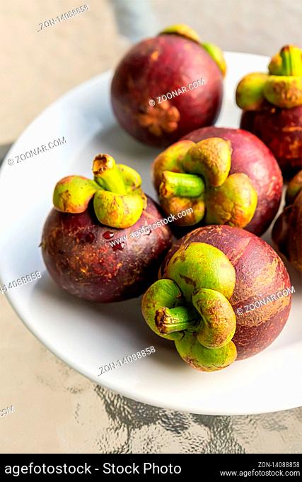 fresh mangosteen whole fruit lies on a white plate close-up vertical photo