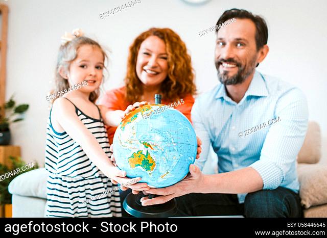 Mom, dad and little girl planning vacation, holding globe. Happy family going on vacation. Image with selective focus