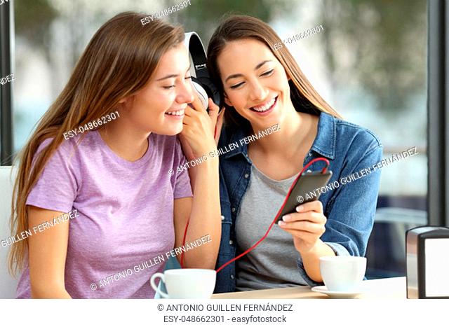 Two happy friends sharing on line music sitting in a bar