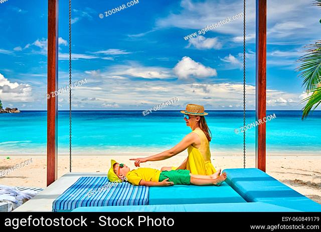 Family on beautiful Petite Anse beach, young woman in yellow with three year old toddler boy. Summer vacation at Seychelles, Mahe