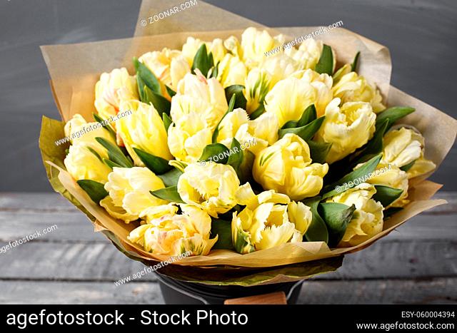 gently yellow pastel colors tulips in vase on wooden table. Gray wall