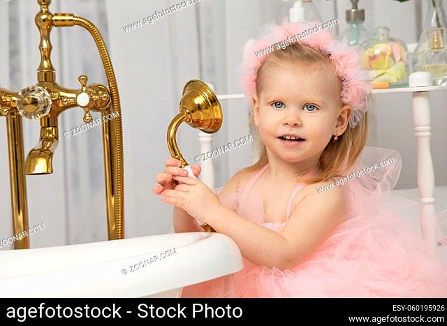 Little funny girl in a smart pink dress in the bathroom