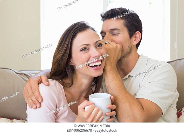 Man whispering secret into a cheerful womans ear in living room