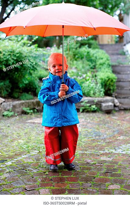 Toddler boy holding umbrella in backyard