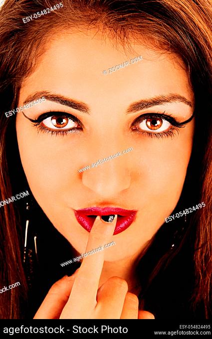 A gorgeous face of a young woman with big eyes and a finger in her mouths with red lips looking at the camera