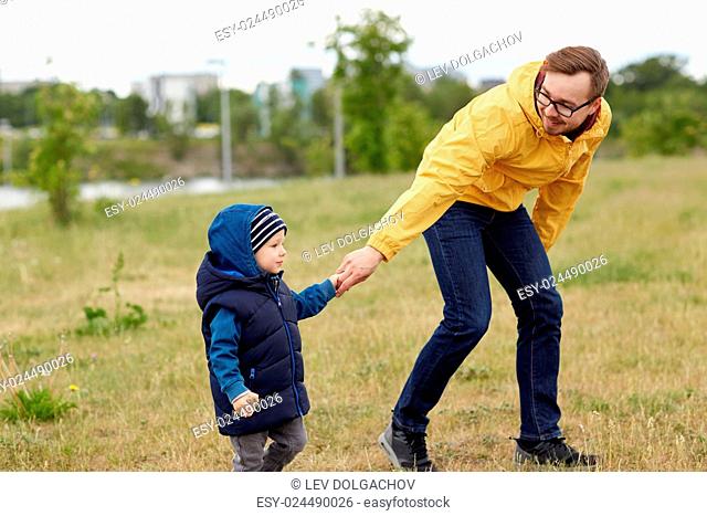 family, childhood, fatherhood, leisure and people concept - happy father and little son walking outdoors