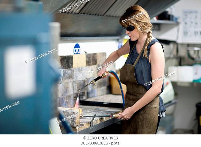Woman wearing safety goggles using blowtorch for metalworking