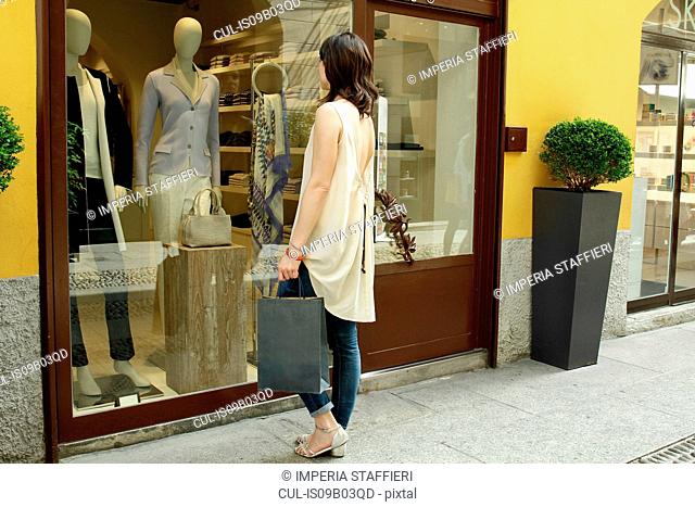 Female shopper looking in boutique window, Milan, Italy