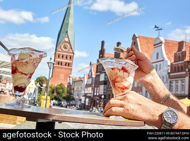 11 August 2023, Lower Saxony, Lüneburg: A man enjoys a large ice cream sundae in a cafe on the square Am Sande on this sunny and warm summer day