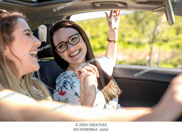 Two women in car, holding hands, laughing