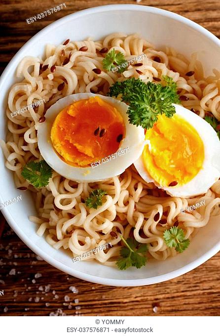 Vertical photo on chinese soup in white bowl full of long noodle, green parsley and nice soft egg slices with orange yolk