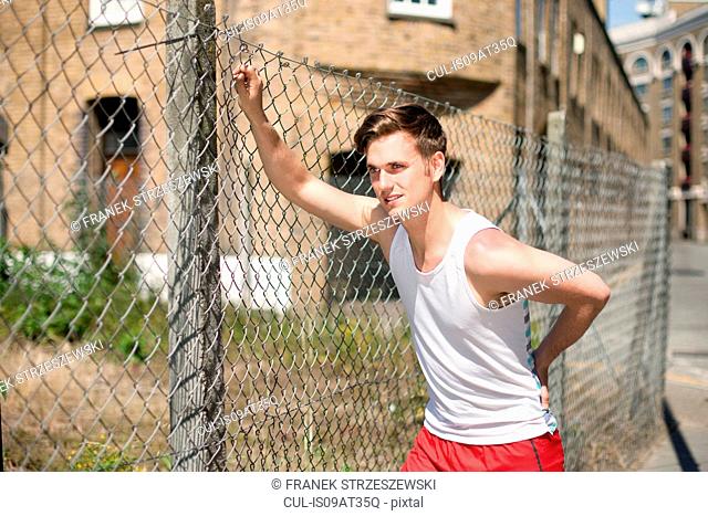 Runner stretching against wire fence, Wapping, London