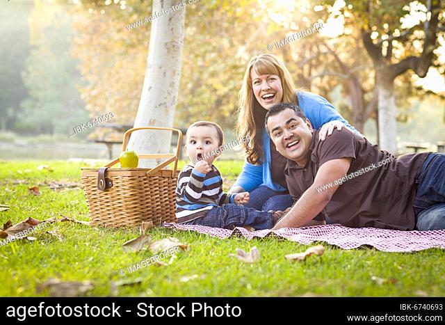 Happy young mixed-race ethnic family having a picnic and playing in the park