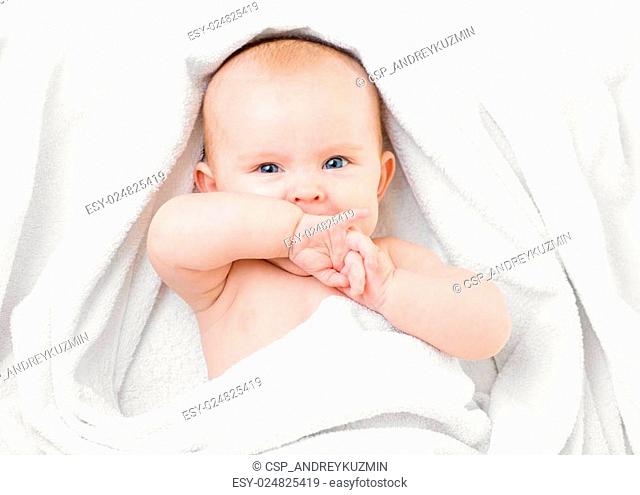 Cute baby lying on white towel and sucking own hand