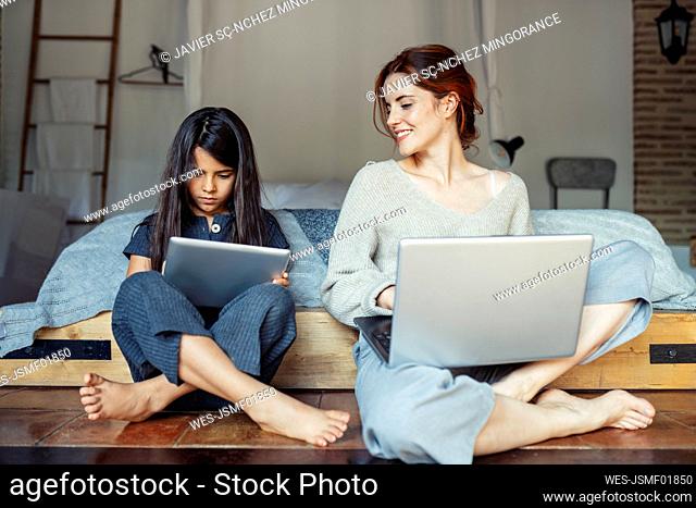 Girl using digital tablet while working on laptop at home
