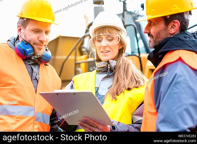 Three workers in a quarry discussing in front of heavy machinery looking at plan